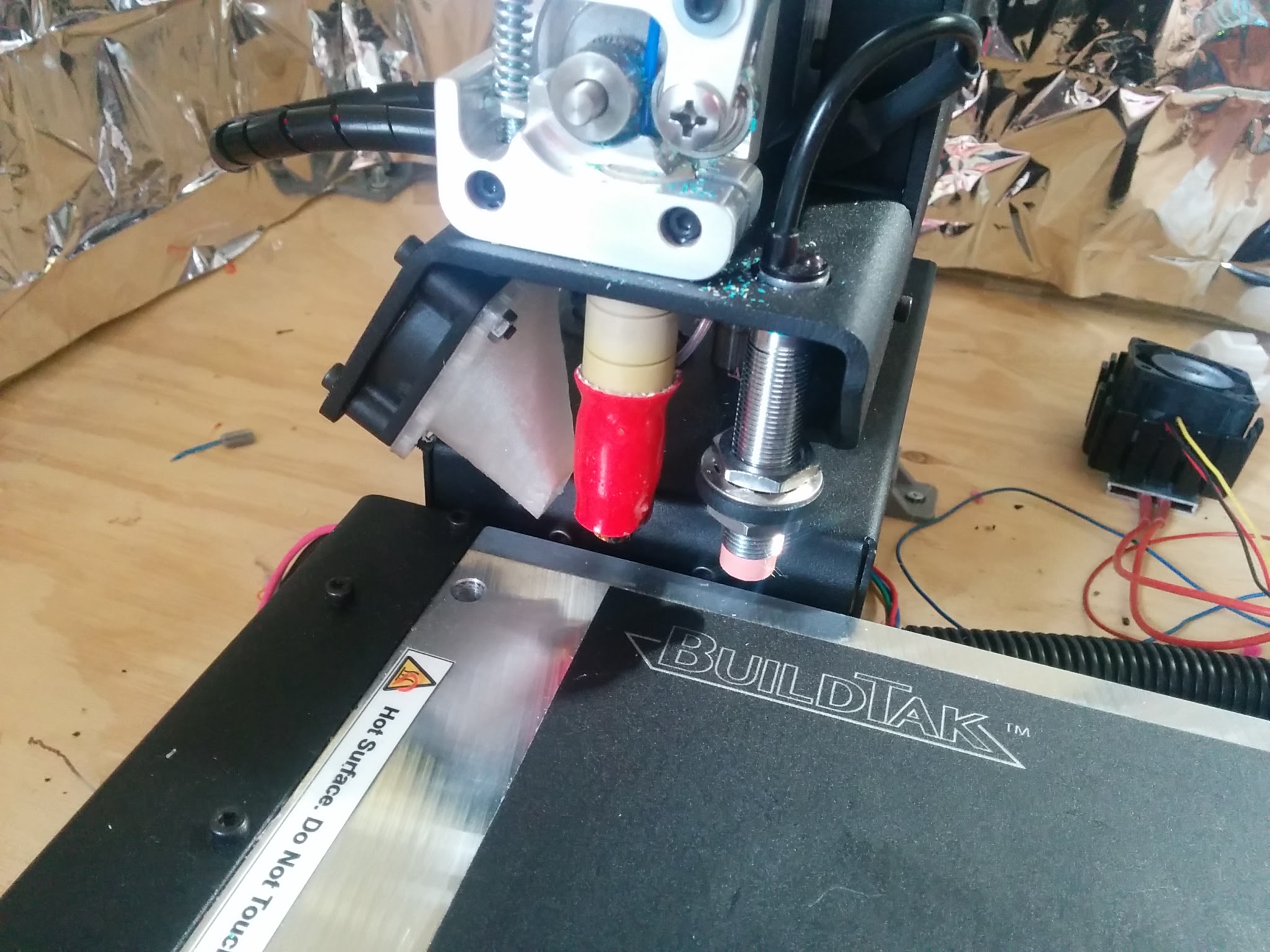 View of the print head. The extruder is the red part in the middle and the inductive sensor is the threaded part on the right. It is positioned to sit just above the bottom of the extruder.